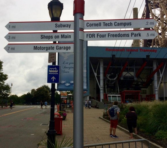 Missed Opportunity: Disappointing Wayfinding Signs Arrive on Roosevelt Island Sign at the Tram Plaza will soon be joined by a kiosk and the RI Welcome Monument. Construction work is visible in the background.